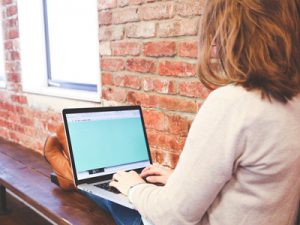 Student sitting near a brick wall with a laptop.