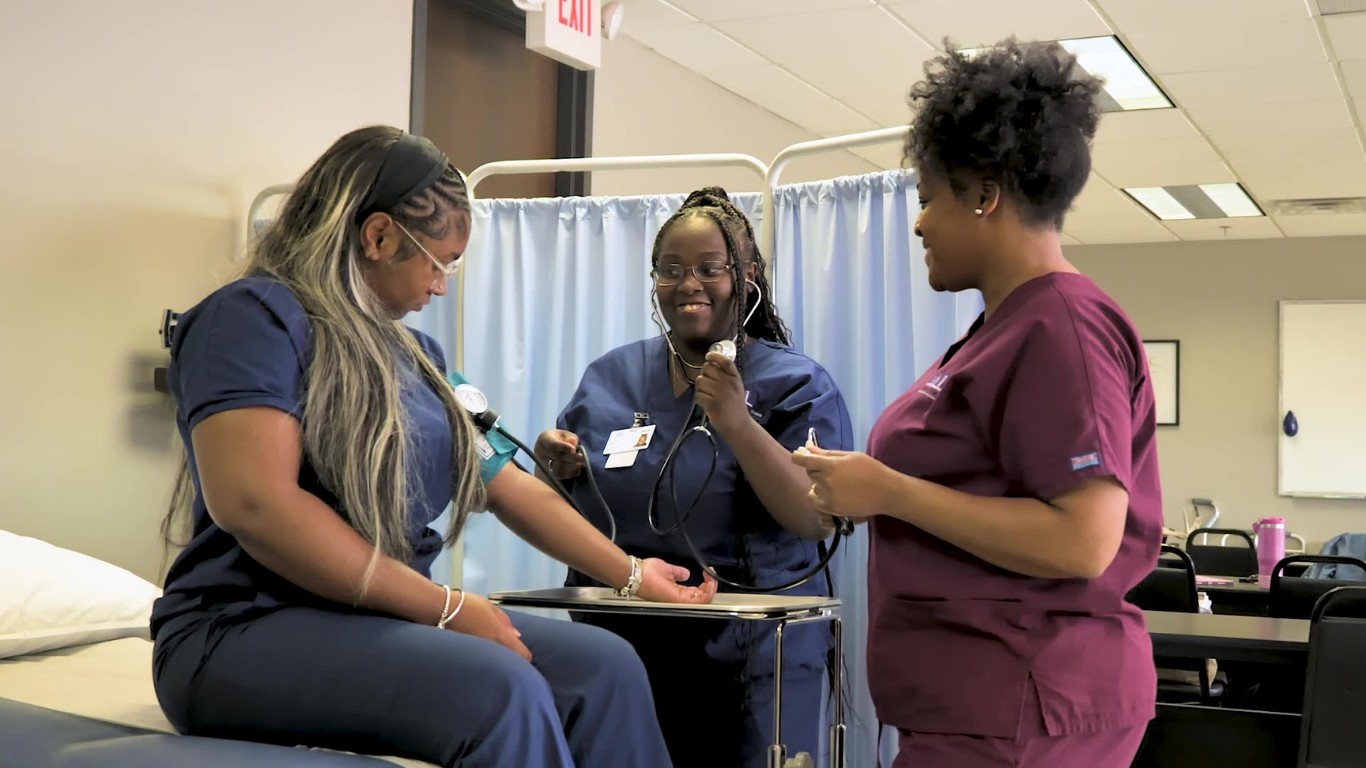 Three medical assistant students in scrubs practice taking a blood pressure reading on each other