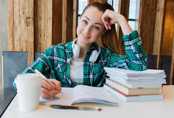 Girl taking notes in a green flannel shirt with her arm resting on a stack of books