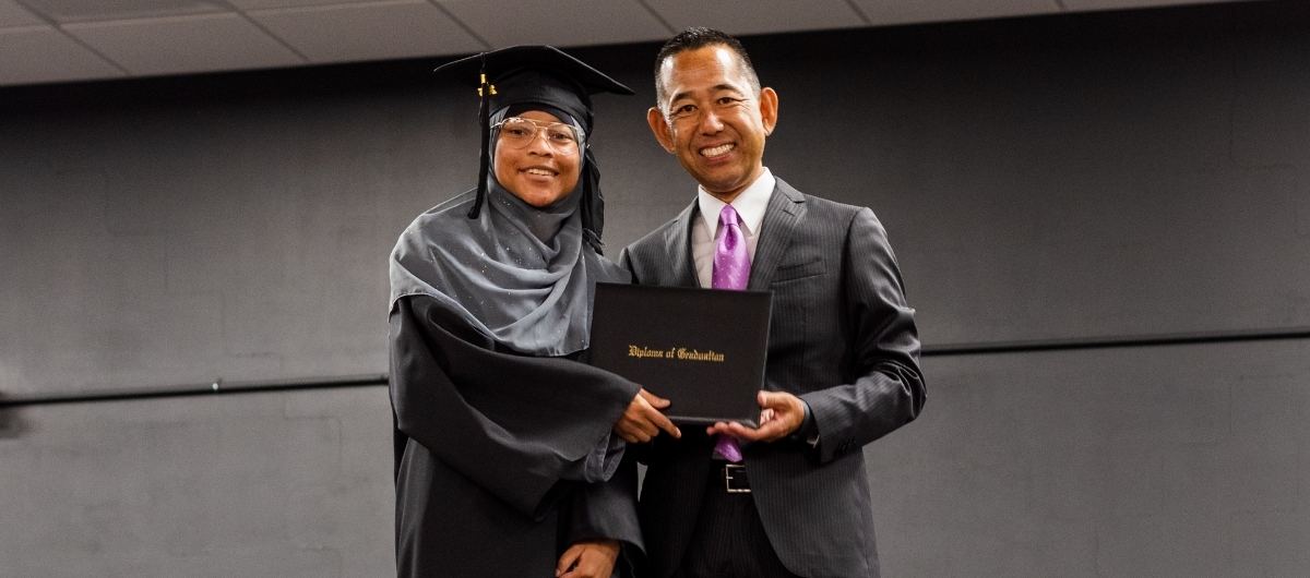 Milwaukee Career College president, Jack Takahashi, stands with vet tech graduate on stage holding diploma and shaking hands.