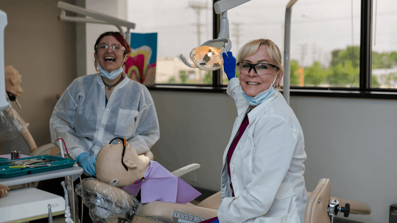 Dental instructor adjusting dentist lamp, student smiling in background